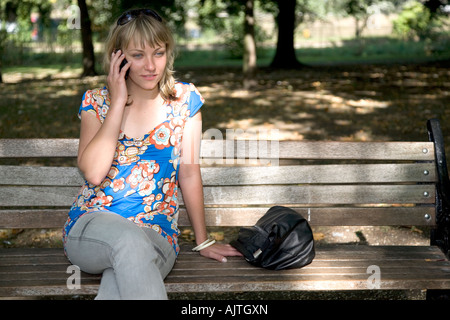 A young woman sat on a park bench, talking on a mobile phone. Stock Photo