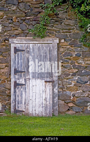 Old barn door set against stones in Delaware Count PA Rusted hinges peeling white paint vines above Stock Photo