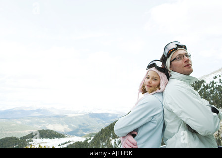 Young man and teen girl skiers standing back to back, smiling, girl looking at camera, portrait Stock Photo