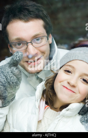 Young man looking over little sister's shoulder and pointing, both smiling at camera, portrait