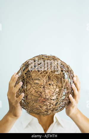 Man holding up wicker sphere in front of face Stock Photo