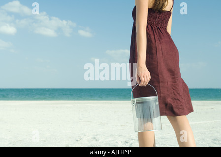 Woman standing on beach, holding bucket, cropped, rear view Stock Photo