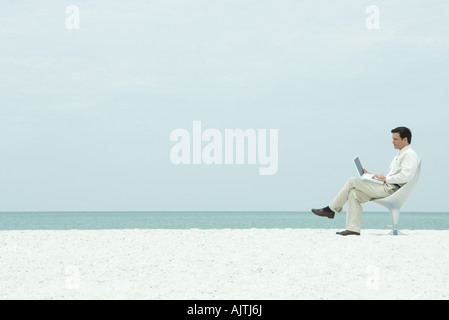 Businessman using laptop computer on the beach, full length Stock Photo