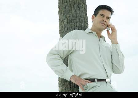 Man leaning against tree trunk, using cell phone, waist up Stock Photo