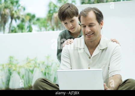 Man using laptop computer, son looking over his shoulder Stock Photo