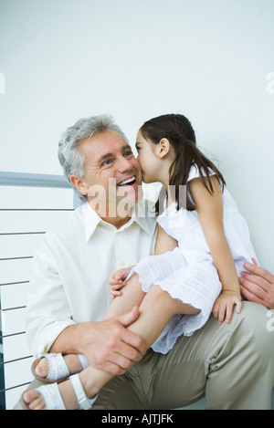 Little girl sitting on mature man's lap, kissing his cheek Stock Photo