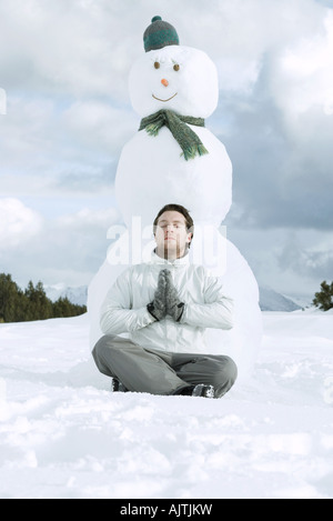 Young man meditating in front of snowman Stock Photo