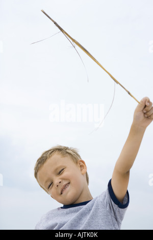 Boy holding up stick, smiling, squinting eyes closed, low angle view Stock Photo