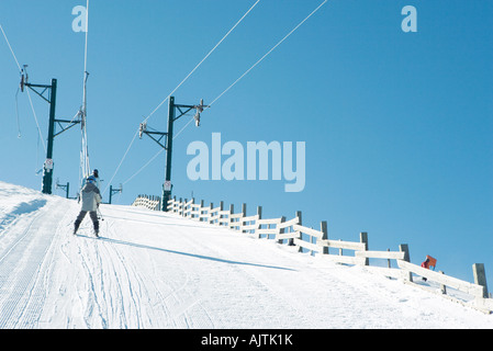 Young skier going up hill on ski lift, rear view Stock Photo