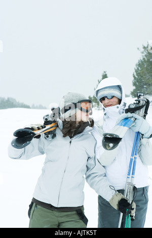 Two young friends carrying skis on shoulders, looking at each other Stock Photo