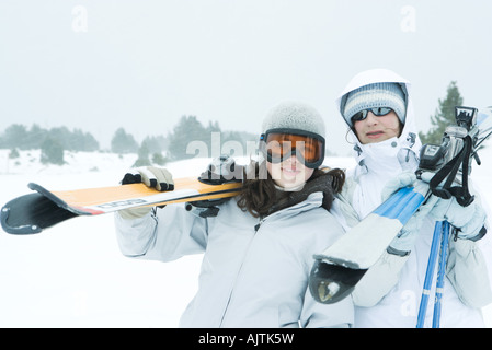 Two young friends carrying skis on shoulders, smiling at camera Stock Photo