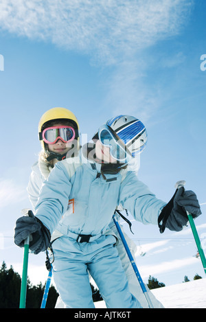 Two young skiers standing, one behind the other, both smiling at camera, low angle view Stock Photo