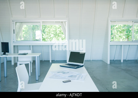 Laptop computer, cell phone, and newspaper on desk in office Stock Photo