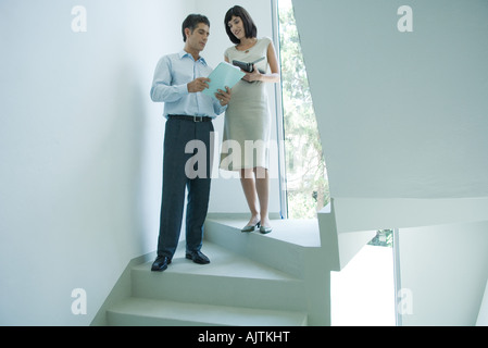 Mature businessman speaking to young female colleague on stairs, showing document Stock Photo
