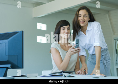 Two female co-workers, one showing the other cell phone Stock Photo
