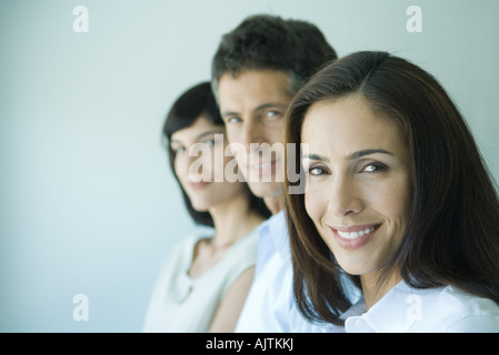 Business team in a row smiling at camera, head and shoulders, focus on woman in foreground, portrait Stock Photo