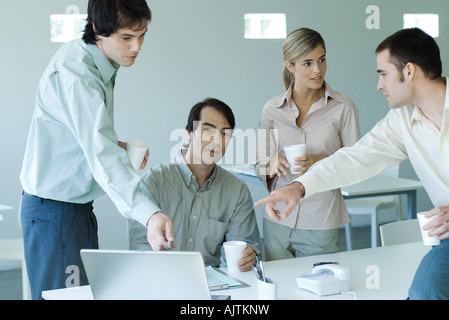Business associates gathered around laptop, two pointing to screen Stock Photo