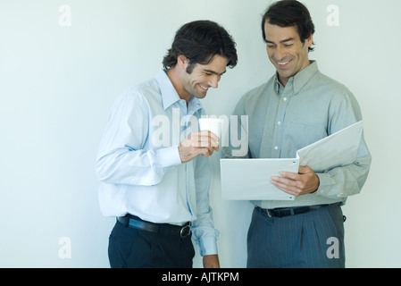 Two male colleagues looking at file together, laughing Stock Photo