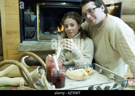 Young man and teen girl drinking hot drinks by fire place Stock Photo