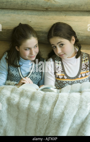 Two teen girls in winter clothes sitting under warm blanket together Stock Photo