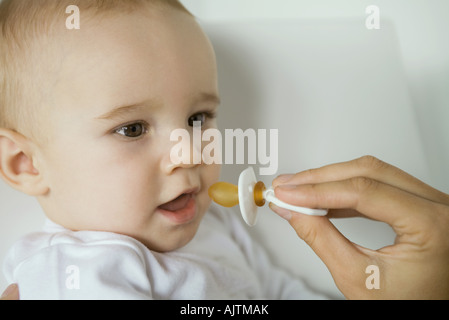 Mother's hand holding up pacifier for baby Stock Photo