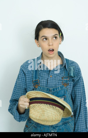 Teenage girl looking up, wide eyes, open mouth, holding hat Stock Photo