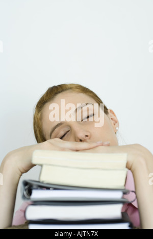 Young woman leaning on stack of books, eyes closed
