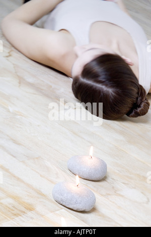 Woman lying on back on the floor, burning candles in foreground Stock Photo