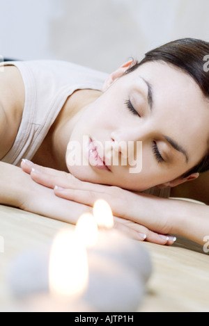 Woman reclining next to burning candles, head resting on arms, eyes closed Stock Photo