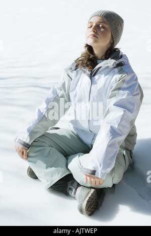 Teenage girl sitting indian style on snow with eyes closed and head back, full length Stock Photo