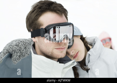 Young man standing with snowboard, little sister resting head on his shoulder