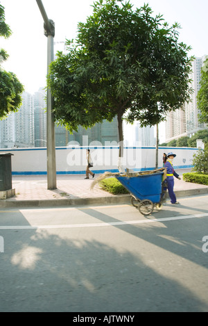 China, Guangdong Province, Guangzhou, public maintenance worker pulling bin through street Stock Photo
