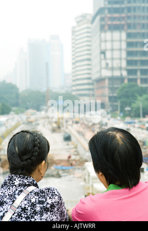 China, Guangdong Province, Guangzhou, two people looking out over construction site, rear view, close-up Stock Photo