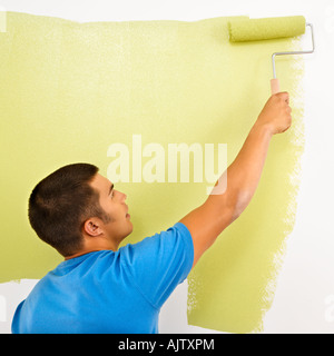 Man painting over white wall with green paint using paint roller Stock Photo