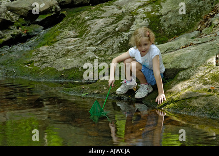 Young girl with net looking to catch frogs or fish in a stream in the woods Stock Photo