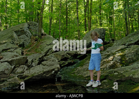 Young girl looking in net for aquatic animals at a stream in the woods Stock Photo