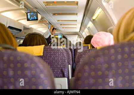 Horizontal wide angle of the interior of an aeroplane cabin with the air steward assisting a passenger. Stock Photo