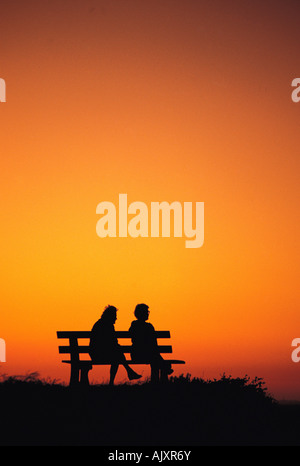 Silhouette of two old women sitting on park bench at sunset. Stock Photo