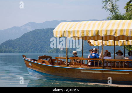 Lake Bled in summer with tourists on traditional wooden pletnja rowing boat trip to St Mary's church island. Bled Slovenia. Stock Photo