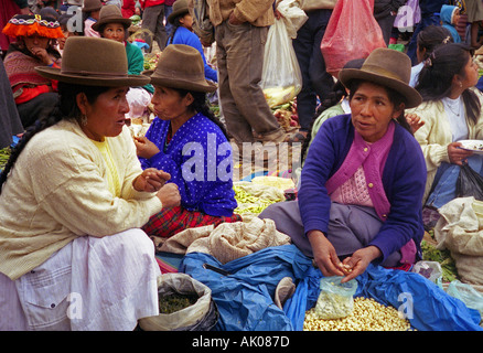 Indigenous peasant women in traditional colourful clothing hat sit sell bean root vegetable Pisac Peru South Latin America Stock Photo
