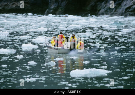 A small boat filled with visitors from a larger cruise ship navigates the iceberg flow beneath a massive glacier Stock Photo
