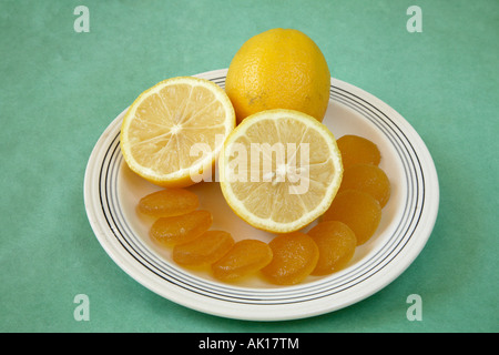 Whole lemon with two cut lemon halves with a crescent of circular yellow lemon jelly candies in front Stock Photo