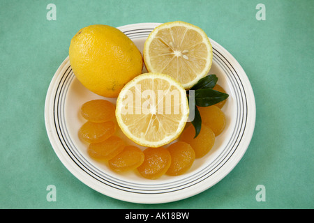 Whole lemon with two cut lemon halves with a crescent of circular yellow lemon jelly candies in front plus a sprig of greenery. Stock Photo