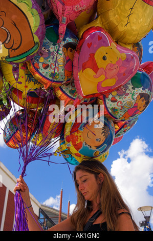Woman street vendor of colourful helium character balloons with smiling faces against blue sky Stock Photo
