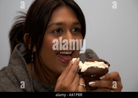 asian girl sitting in coffee shop eating a chocolate muffin filled with fresh cream Stock Photo