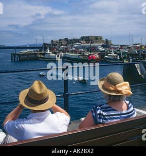 A shoulder high back view of couple on bench watching moored fishing boats at Castel Cornet in St Peter Port Guernsey Stock Photo