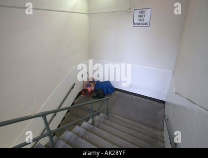 Homeless person in city subway stairwell under bright lights and surveillance video camera in San Francisco California USA Stock Photo