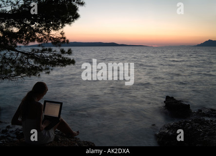 Woman Using a Laptop Computer on the Seashore at Dusk Stock Photo