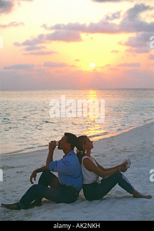 Maldives. Young couple relaxing on tropical beach at sunset. Stock Photo