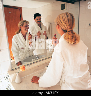 Mirror reflection of man and woman wearing white bathrobes in hotel bathroom. Stock Photo